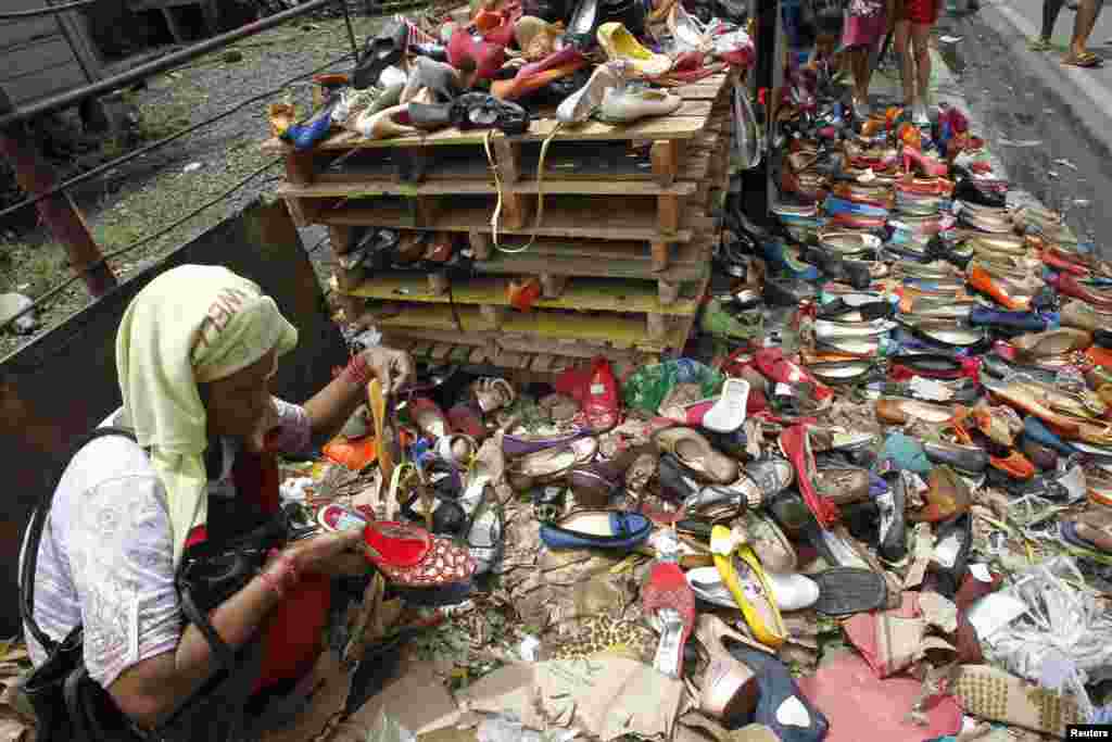 Seorang perempuan mengamati sepatu-sepatu yang rusak akibat banjir yang diobral seharga 10 peso (Rp 2400) sepasang di daerah kumuh di Manila, Filipina.