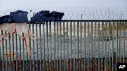 FILE - A man sleeps next to the U.S. border wall topped with razor wire in Tijuana, Mexico, June 9, 2019.
