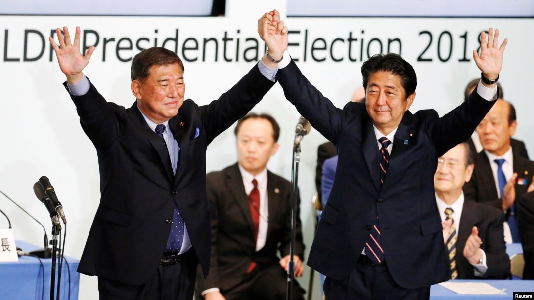Perdana Menteri Jepang, Shinzo Abe (kanan) yang juga pemimpin Partai Yang Berkuasa, Partai Demokratik Liberal, mengangkat tangannya bersama mantan Menhan Shigeru Ishiba pasca diumumkannya kemenangan Abe sebagai pemimpin partai melalui pemungutan suara di markas besarnya di Tokyo, 20 September 2018.