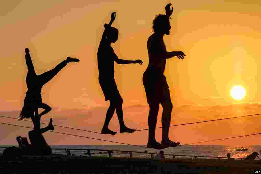 People walk on a tightrope along the Mediterranean sea waterfront in Tel Aviv at sunset.