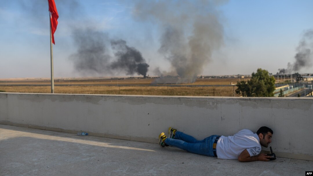 A journalist takes cover in Akcakale near the Turkish border with Syria, Oct. 10, 2019, as a mortar lands nearby on the second day of Turkey's military operation against Kurdish forces.