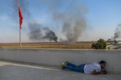 A journalist takes cover in Akcakale near the Turkish border with Syria, Oct. 10, 2019, as a mortar lands nearby on the second day of Turkey's military operation against Kurdish forces.