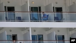 In this May 8, 2020 photo, people aboard the Norwegian Epic cruise ship docked at PortMiami in Miami, sit on their balconies. Tens of thousands of crew members, including U.S. citizens, remain confined to cabins aboard cruise ship.