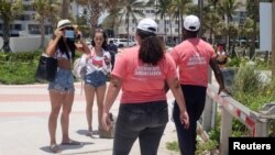 Una mujer se pone la máscara de protección bajo la indicación de los "Embajadores del distanciamiento social" en las áreas reabiertas de una playa de Miami. Junio 10 de 2020.