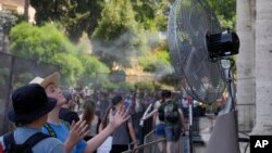 ARCHIVO: Turistas se refrescan frente a un ventilador eléctrico en la entrada del Coliseo de Roma el 18 de julio de 2023.