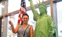 La nueva ciudadana estadounidense Doris Nazarian ondea la bandera mientras posa junto a una réplica de la Estatua de la Libertad durante una ceremonia de naturalización antes del Día Mundial del Refugiado.