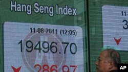 A man walks past a panel displaying the Hang Seng Index during a midday break, outside a bank in Hong Kong, August 11, 2011