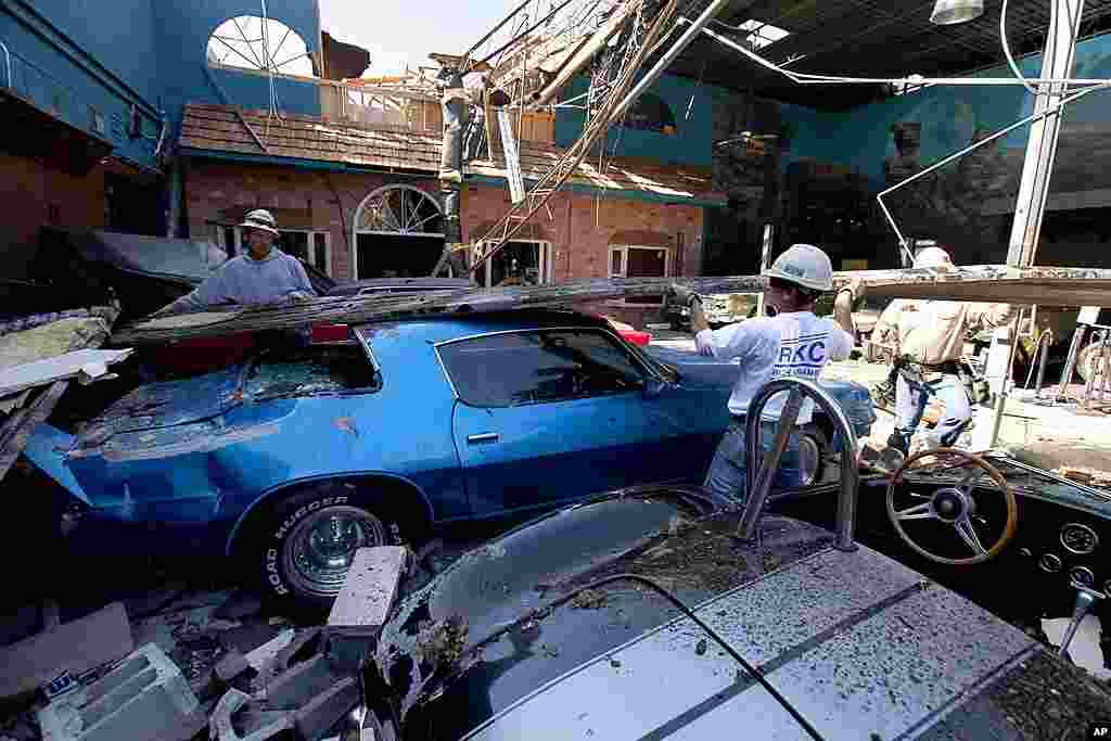 Construction workers lift a piece of sheet metal off of classic cars in a storm-damaged display room at Branson Auto World in Branson, Missouri, February 29, 2012. (AP) 