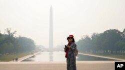 A tourist looks on as haze blankets over the Washington Monument seen at a distance, Wednesday, June 7, 2023, in Washington. Smoke from Canadian wildfires is pouring into the U.S. East Coast and Midwest and covering the capitals of both nations in an unhealthy haze. (AP Photo/Julio Cortez)