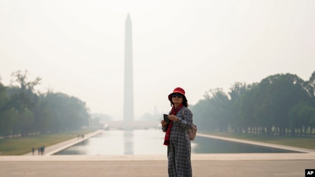 A tourist looks on as haze blankets over the Washington Monument seen at a distance, Wednesday, June 7, 2023, in Washington. Smoke from Canadian wildfires is pouring into the U.S. East Coast and Midwest and covering the capitals of both nations in an unhealthy haze. (AP Photo/Julio Cortez)