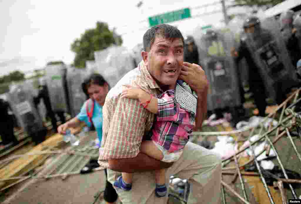 A Honduran migrant protects his child after fellow migrants stormed a border checkpoint in Guatemala, in Ciudad Hidalgo, Mexico, Oct. 19, 2018.