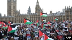 Protesters hold placards and wave Palestinian flags as they walk over Westminster Bridge with the Palace of Westminster, home of the Houses of Parliament behind during a 'March For Palestine' in London on October 28, 2023, to call for a ceasefire in the c