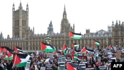 Protesters hold placards and wave Palestinian flags as they walk over Westminster Bridge with the Palace of Westminster, home of the Houses of Parliament, behind them in London on Oct. 28, 2023.