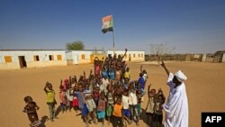 FILE - Displaced Sudanese children gather under the national flag in a school yard, Feb. 1, 2021. Six children died after a metal device exploded near a refugee settlement in northwestern Uganda.