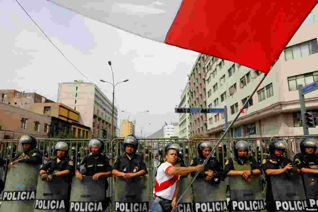 Un hombre ondea una bandera mientras los policías montan guardia durante una protesta después de que el Congreso aprobara la destitución del presidente Pedro Castillo, en Lima, Perú, el 7 de diciembre de 2022. REUTERS/Alessandro Cinque