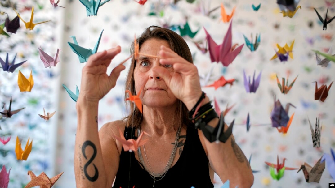 Karla Funderburk, seniman dan pemilik Matter Studio Gallery, di Los Angeles, AS, menata salah satu dari ribuan origami yang digantungnya dalam pameran yang digelar untuk menghormati para korban Covid-19, Selasa, 11 Agustus 2020. (Foto: dok).