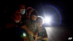 FILE - In this May 17, 2021, file photo a group of migrants mainly from Honduras and Nicaragua wait along a road after turning themselves in upon crossing the U.S.-Mexico border, in La Joya, Texas. 