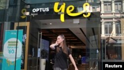 FILE - A woman uses her mobile phone as she walks past in front of an Optus shop in Sydney, Australia, Feb. 8, 2018. 