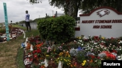 FILE - Chad Williams, 19, a survivor of the Marjory Stoneman Douglas High School shooting, stands alone at a memorial garden outside the school in Parkland, Fla., March 16, 2019.