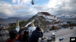 FILE - Tourists take photos of the Potala Palace beneath a security camera in Lhasa, capital of the Tibet Autonomous Region of China, Sept. 19, 2015. 