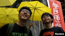 Student leaders Joshua Wong (R) and Nathan Law smile in front of supporters holding yellow umbrellas, symbol of the Occupy Central movement, outside a police station in Hong Kong, July 14, 2015.