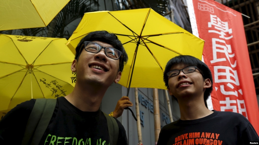 Pemimpin mahasiswa Hong Kong, Joshua Wong (kanan) dan Nathan Law di depan para pendukung yang memegang payung kuning, simbol gerakan Occupy Central movement, di luar kantor polisi di Hong Kong, 14 Juli 2015.
