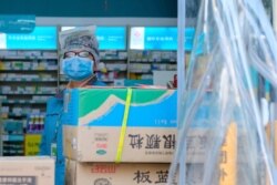 A clerk wearing a face mask and a plastic bag stands in a pharmacy in Wuhan in central China's Hubei Province, Jan. 31, 2020.