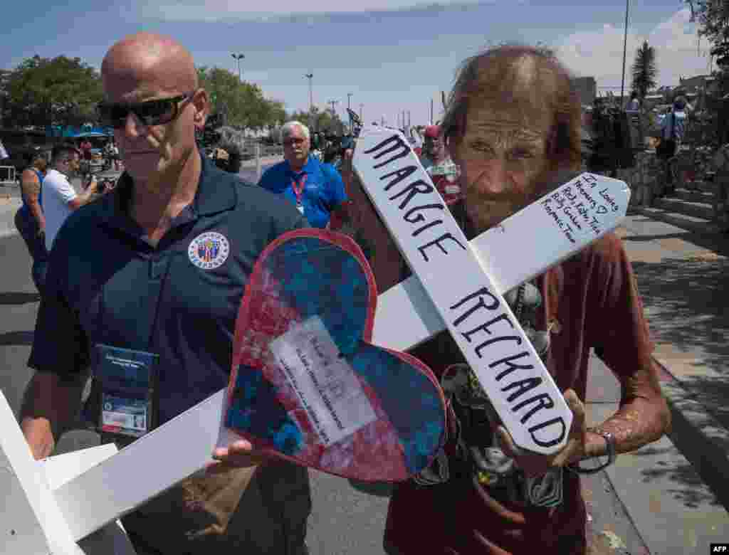 Antonio Basbo (R) holds the cross of his common-law wife Margie Reckard who died in the shooting as he walks to a makeshift memorial in El Paso, Texas, Aug. 5, 2019, two days after the shooting that left 22 people dead at the Cielo Vista Mall WalMart.