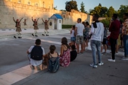 FILE - Tourists look at the changing of presidential guards outside the Greek parliament , in Athens, July 31, 2020.