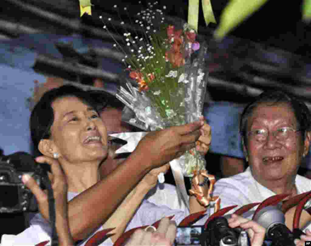 Burma's pro-democracy leader Aung San Suu Kyi smiles after she received flowers from her supporters as she stands at the gate of her home in Rangoon, 13 Nov 2010.