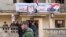 FILE - A Syrian police officer walks past a group of local people standing at a building with a portrait of Syrian President Bashar al-Assad in Salma, Syria, Jan. 22, 2016.  