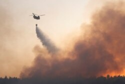 A helicopter makes a water drop as a wildfire continues to rage in Varympompi suburb, north of Athens, Greece, August 4, 2021.