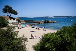 FILE - People swim and enjoy a sunny day at 'Les Cigales' beach in Port-Grimaud, with Saint-Tropez in the background, southern France on July 10, 2021.