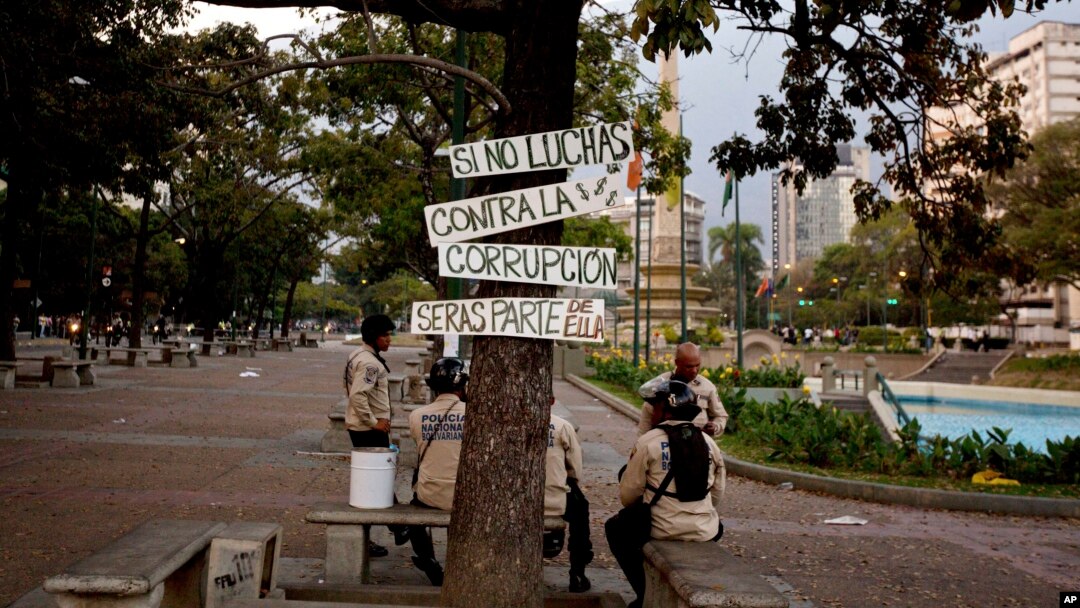 Miembros de la guardia bolivariana descansan a la sombra de un árbol con rótulos anticorrupción en Caracas.