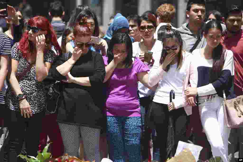 Para pegawai Lindt Cafe memberi penghormatan pada para kolega mereka yang kehilangan nyawanya menyusul penembakan dalam kasus penyanderaan, di memorial di Martin Place, distrik bisnis di Sydney, Australia (16/12). (AP/Steve Christo)