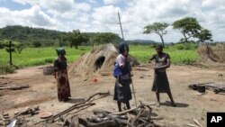 Members of a family stand next to their grass-hut dwelling which was destroyed by the police at Manzou Farm in Mazoe, north of Harare, in Zimbabwe, Jan. 15, 2015.