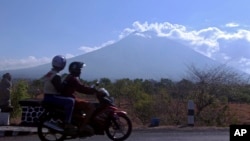 Motorists ride past Mount Agung volcano, seen in the background, in Karangasem, Bali, Indonesia, Sept. 28, 2017. Warnings that the volcano on the tourist island will erupt have sparked an exodus as authorities have ordered the evacuation of villagers living within a high danger zone that in places extends 12 kilometers (7.5 miles) from its crater.