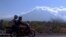 Motorists ride past Mount Agung volcano, seen in the background, in Karangasem, Bali, Indonesia, Sept. 28, 2017. Warnings that the volcano on the tourist island will erupt have sparked an exodus as authorities have ordered the evacuation of villagers living within a high danger zone that in places extends 12 kilometers (7.5 miles) from its crater.