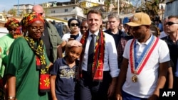 Presiden Prancis Emmanuel Macron (tengah) berjalan bersama sejumlah warga lokal saat berkunjung ke distrik kavani di Mamoudzou, Mayotte, pada 19 Desember 2024, menyusul topan yang memporak-porandakan wilayah tersebut. (Foto: Ludovic Marin/Pool/AFP)