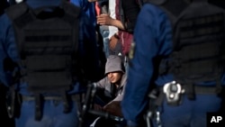 FILE - A man sits on the side of a road as he and a group of migrants and refugees are surrounded by Hungarian police officers in Roszke, Hungary, Sept. 7, 2015.