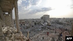 FILE - Syrians gather amidst destruction in Zardana, in the mostly rebel-held northern Syrian Idlib province, in the aftermath of airstrikes in the area, June 8, 2018.