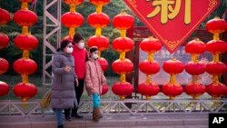 Personas con máscaras médicas posan para la foto frente a decoraciones de una feria de un templo cancelada con motivo del Año Nuevo Lunar en el Parque Longtan, en Beijing, el sábado 25 de enero de 2020. (AP Foto/Mark Schiefelbein)