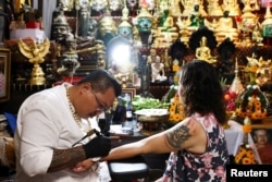 Tattoo master Seeharat Muenyant works on a magic tattoo on the forearm of 56-year-old Kamonwan Patimahongthong, of the pattern of the famous Pop Mart's Labubu monster, which is believed to have mystical power and bring good fortune, in Nonthaburi province on the outskirts of Bangkok, Thailand, June 12, 2024. REUTERS/Chalinee Thirasupa