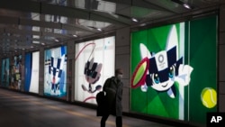 A man with a protective mask walks past large displays promoting the Tokyo 2020 Olympics, Feb. 24, 2020, in Tokyo, Japan.