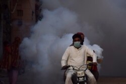 Health workers on motor-bike fumigate, as a preventive measure against coronavirus, along a street in Hyderabad, Pakistan, March 15, 2020.