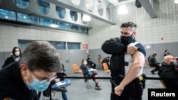 FILE - A member of the New York Police Department rolls up his sleeve before receiving a dose of the Moderna COVID-19 vaccination at Queens Police Academy in the Queens borough of New York, Jan. 11, 2021. 