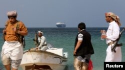 (FILE) Armed men stand on the beach as a commercial ship, seized by Yemen's Houthis, is anchored off the coast.