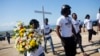 FILE - Youths of Cite Soleil carry flowers and a cross to a monument honoring the victims of the 2010 earthquake before a memorial service at Titanyen, a mass burial site north of Port-au-Prince, Haiti, Jan. 12, 2019.