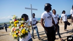 FILE - Youths of Cite Soleil carry flowers and a cross to a monument honoring the victims of the 2010 earthquake before a memorial service at Titanyen, a mass burial site north of Port-au-Prince, Haiti, Jan. 12, 2019.