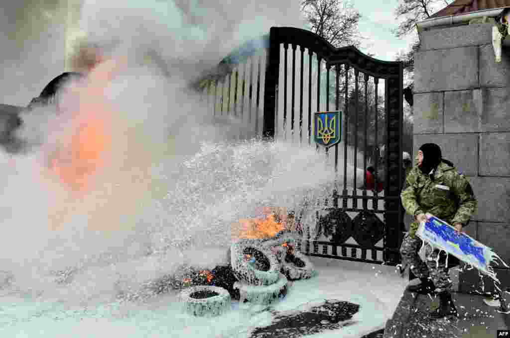 A Ukrainian serviceman throws a signboard over the gates as the flames are doused after fighters of the Aydar Ukrainian volunteer battalion, burn tires at the entrance to the Defense Ministry in Kyiv during a protest against the possible disbandment of their battalion.